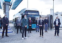 Mehrere Herren stehen vor einem Wasserstoffbus der Autokraft und einer Wasserstofftankstelle. Der Bus ist eFarm-Petrol und die Herren tragen Jackett und Krawatte.