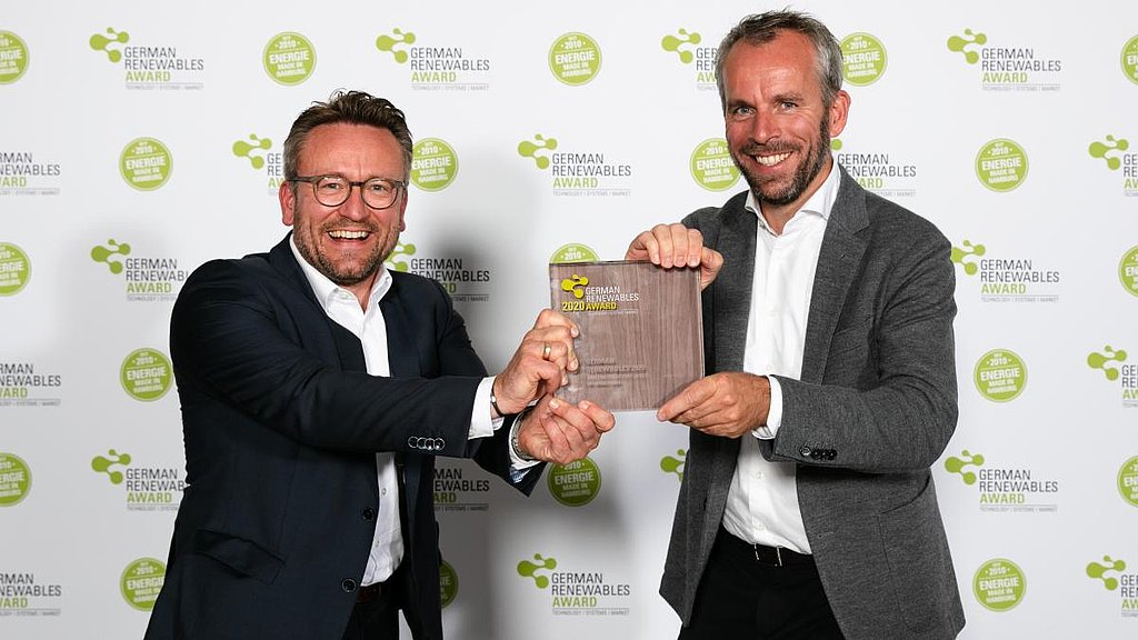 Im Bild stehen zwei Herren (André Steinau und Ove Petersen) je im Anzug und halten lächeln dden German Renewables Award in der Kategorie Projekt des Jahres fest. Im Hintergrund ist das Logo des German Renewables Awards mehrfach abgebildet. 